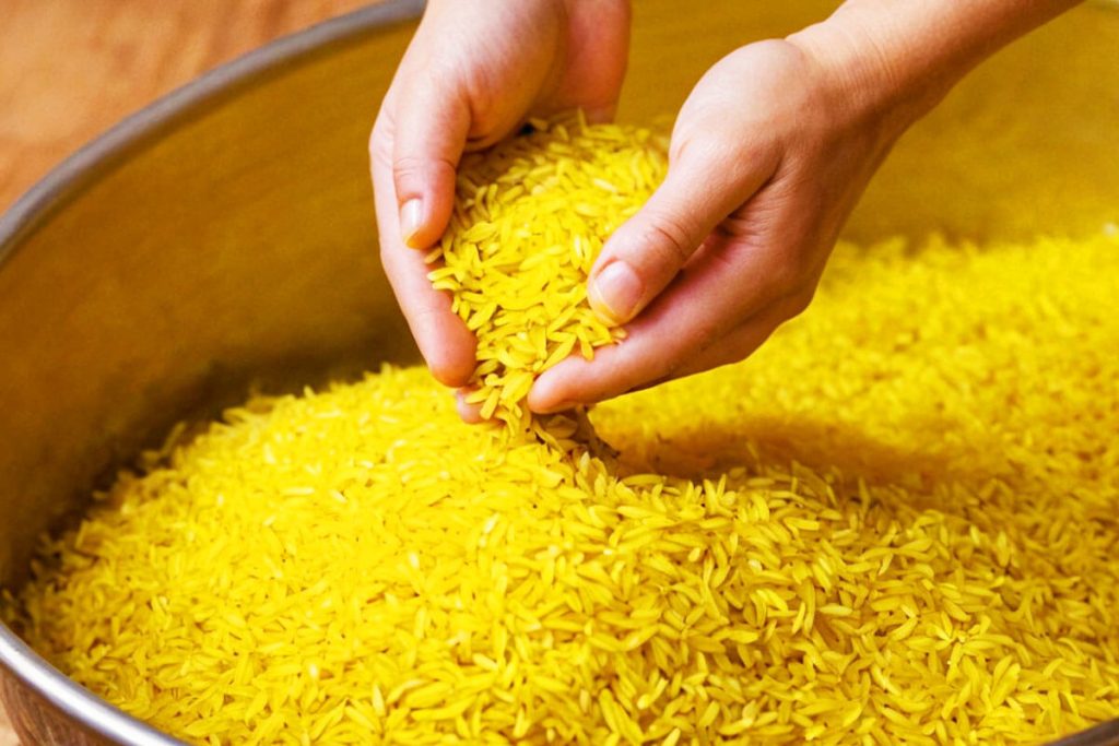 A chef's hand gently rinsing yellow rice under a stream of water.