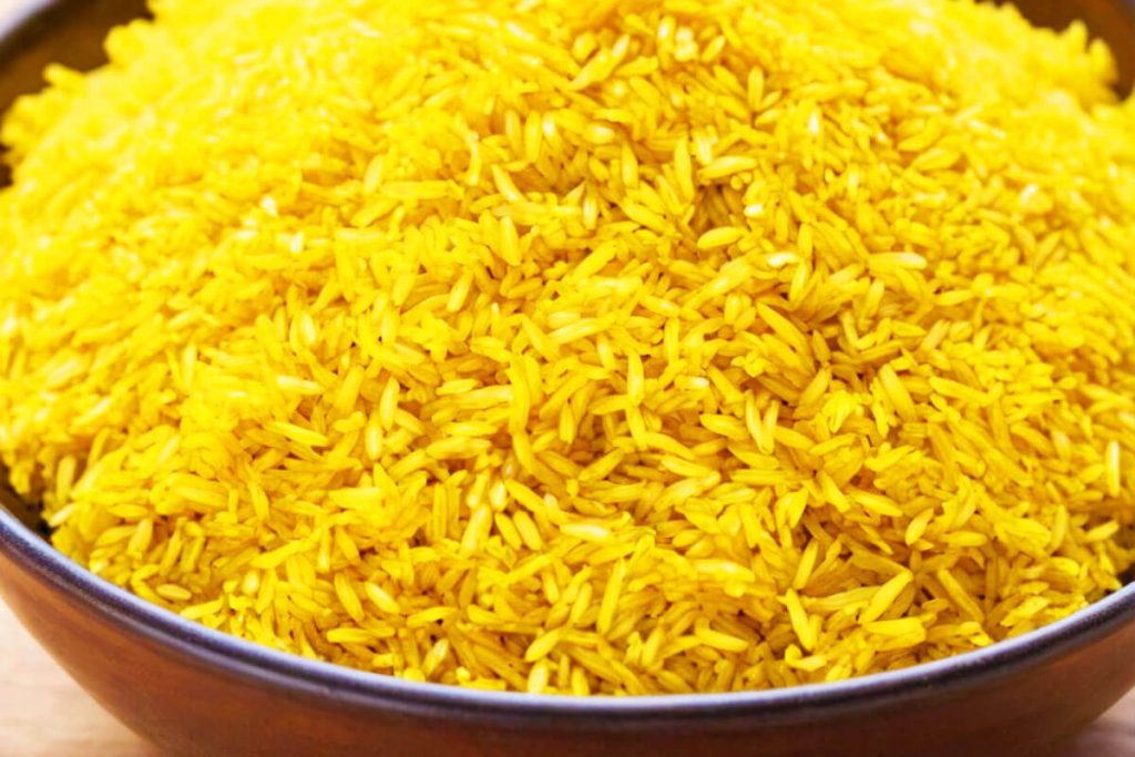 A bowl of vibrant yellow rice garnished with parsley leaves.