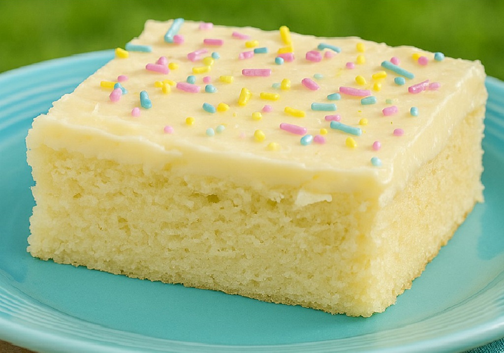 Slice of moist vanilla cake with fluffy buttercream frosting on a white plate