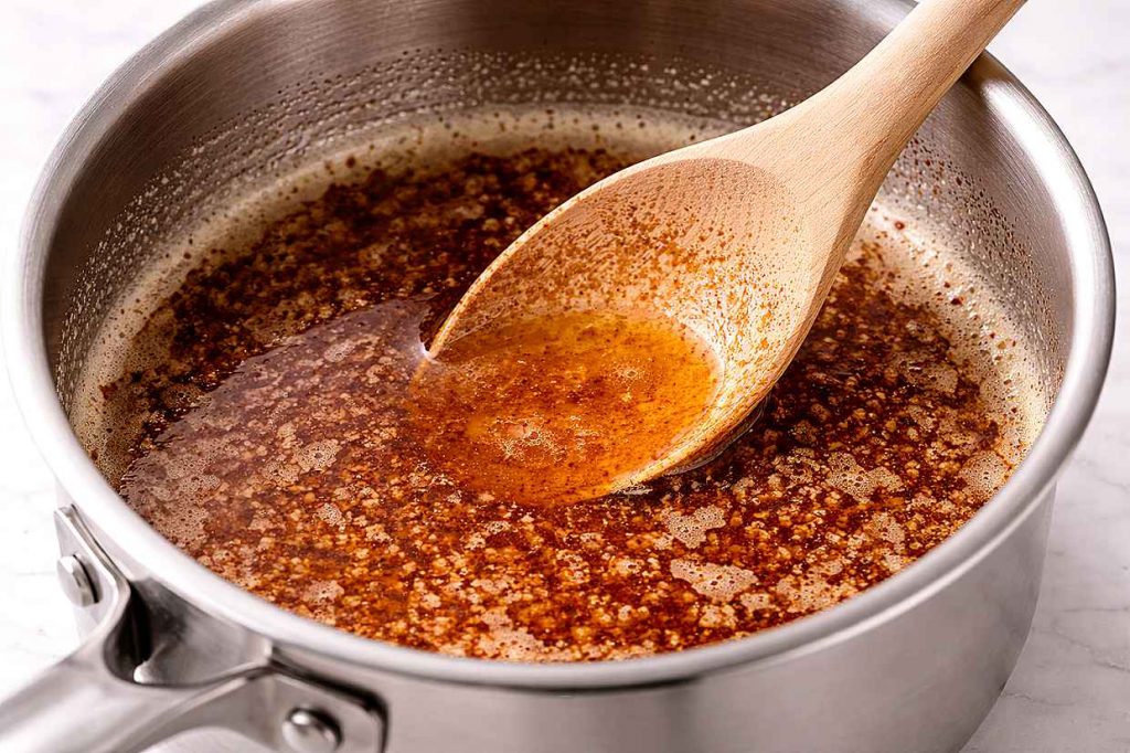 Small saucepan with brown butter at the nutty golden stage with visible golden milk solids on a white kitchen surface