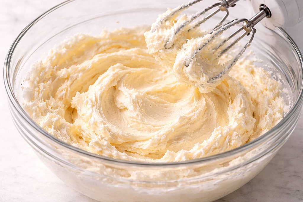 Pale fluffy creamed butter and sugar in a glass mixing bowl showing the light aerated texture before adding eggs