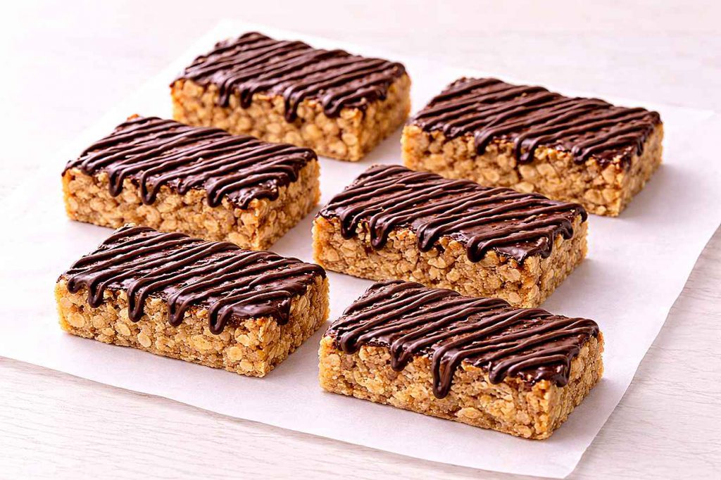 Six no-bake banana oat bars with chocolate drizzle cut into neat rectangles on parchment paper showing the dense oat interior