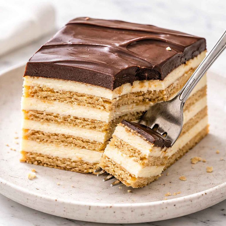Slice of no-bake chocolate eclair cake on a speckled ceramic plate with a fork showing the distinct softened biscuit layers and creamy vanilla filling in cross-section