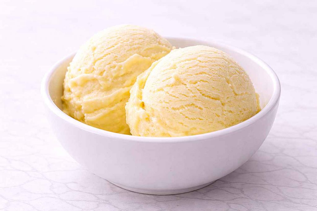 Two scoops of homemade no-churn lemon ice cream in a white ceramic bowl showing the smooth pale yellow texture with no ice crystals