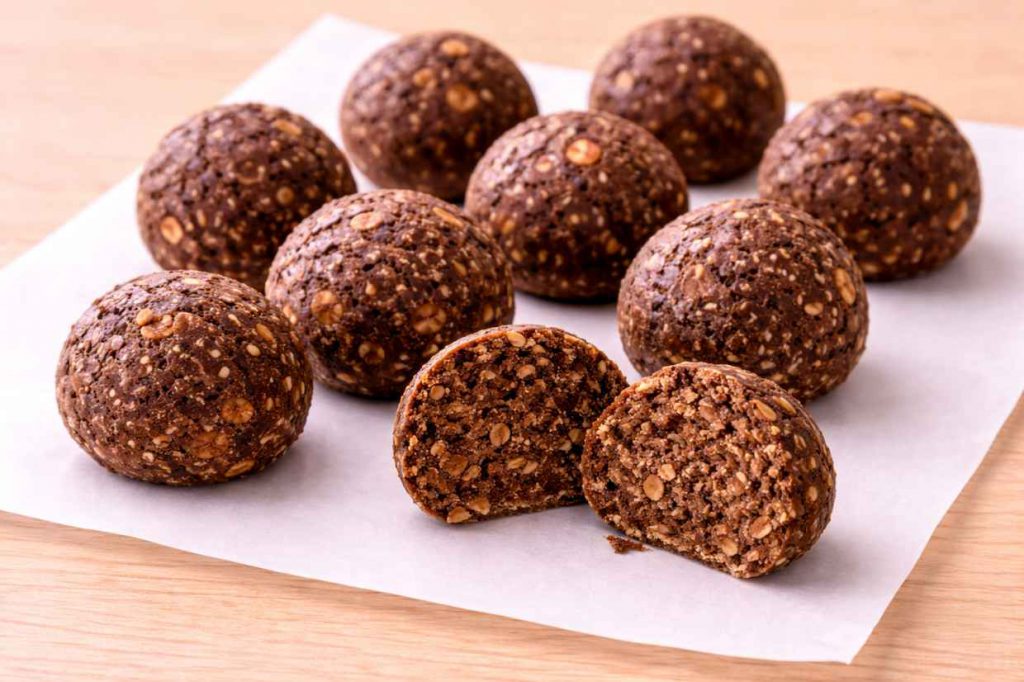 Eight round no-bake chocolate oat energy bites on parchment paper on a wooden surface showing the dense chocolate oat texture